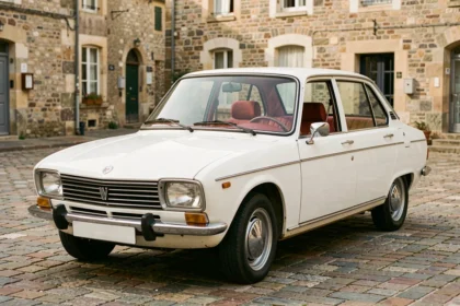 Renault 8 de série blanche garée sur une place de village français, vue de trois quarts avant avec détails chrome et intérieur rouge